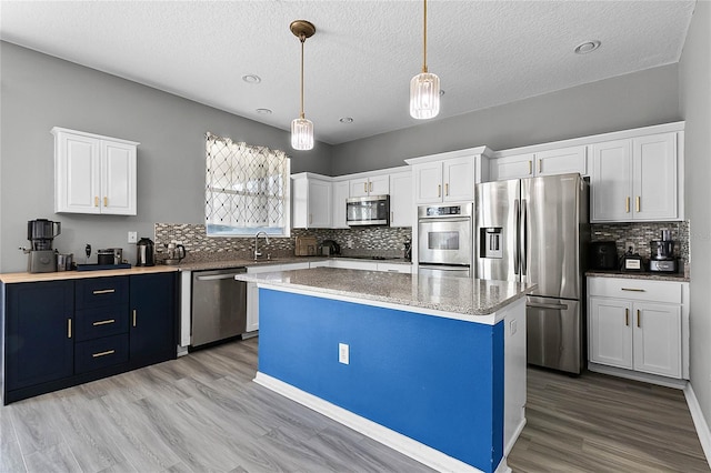 kitchen featuring white cabinetry, hanging light fixtures, light hardwood / wood-style floors, a kitchen island, and appliances with stainless steel finishes