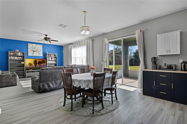 dining room with a textured ceiling, ceiling fan with notable chandelier, and light wood-type flooring