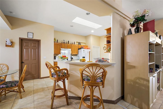 kitchen featuring a kitchen bar, white appliances, kitchen peninsula, and a skylight