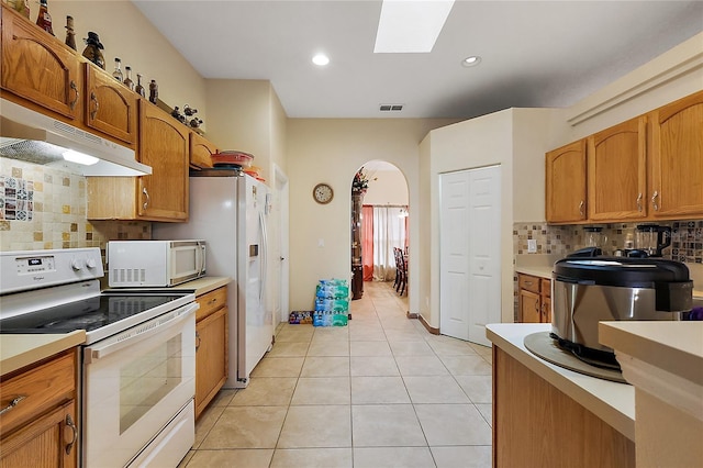 kitchen with decorative backsplash, stove, a skylight, and light tile patterned floors