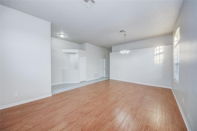 spare room with a chandelier, a textured ceiling, and light wood-type flooring