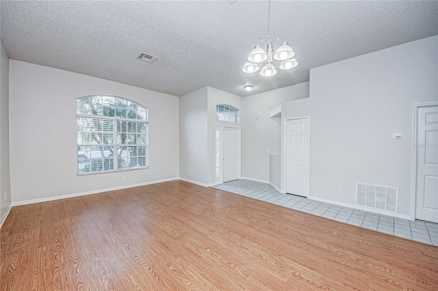 unfurnished room featuring a notable chandelier, light hardwood / wood-style floors, and a textured ceiling