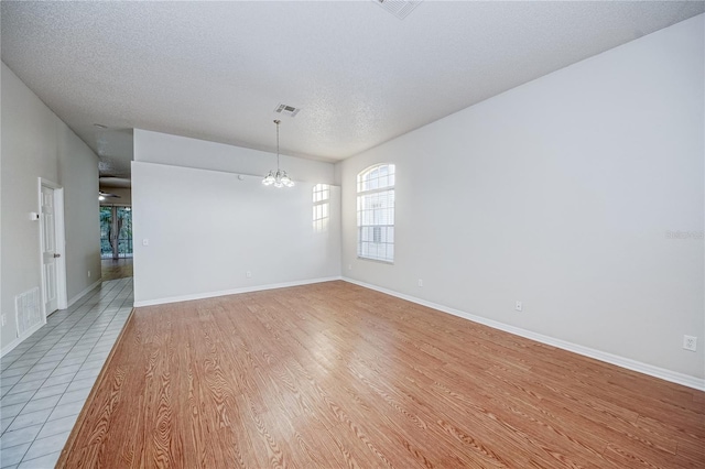 empty room with a chandelier, a textured ceiling, and light wood-type flooring