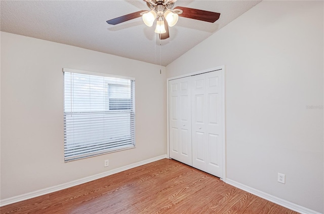 unfurnished bedroom with ceiling fan, light hardwood / wood-style floors, a textured ceiling, vaulted ceiling, and a closet