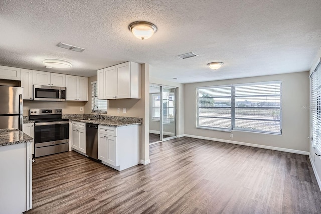 kitchen with dark hardwood / wood-style flooring, dark stone countertops, white cabinetry, and stainless steel appliances