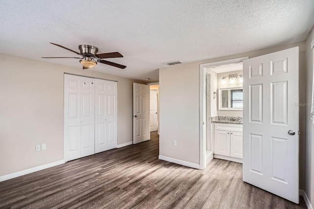 unfurnished bedroom with ceiling fan, dark hardwood / wood-style floors, a textured ceiling, connected bathroom, and a closet