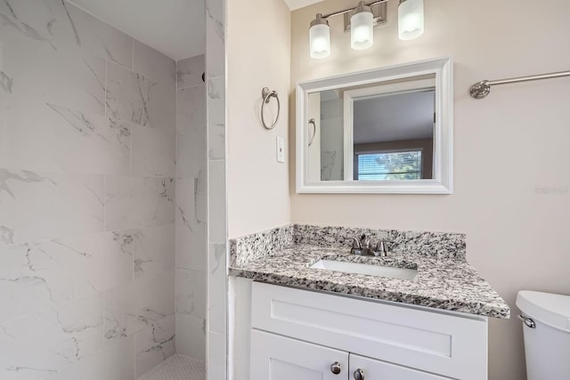 bathroom with a tile shower, vanity, and toilet