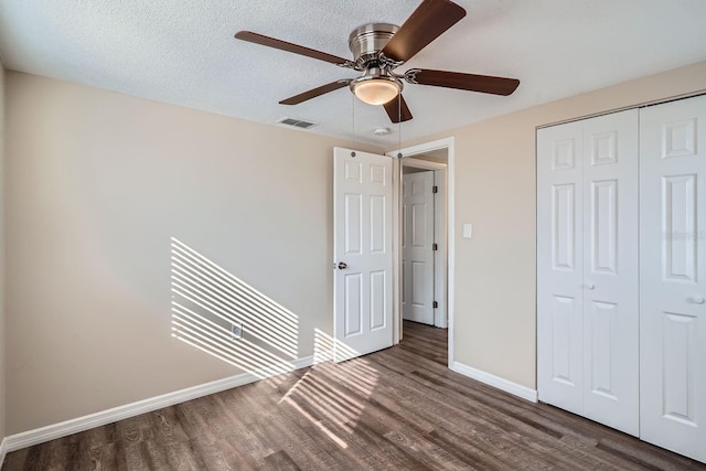 unfurnished bedroom with ceiling fan, a closet, dark wood-type flooring, and a textured ceiling