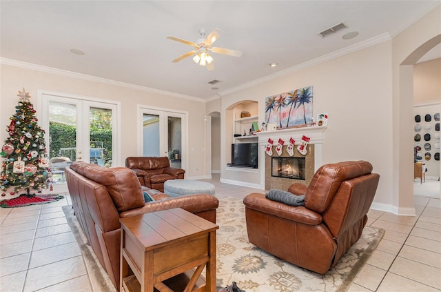 tiled living room featuring built in shelves, ceiling fan, crown molding, and french doors