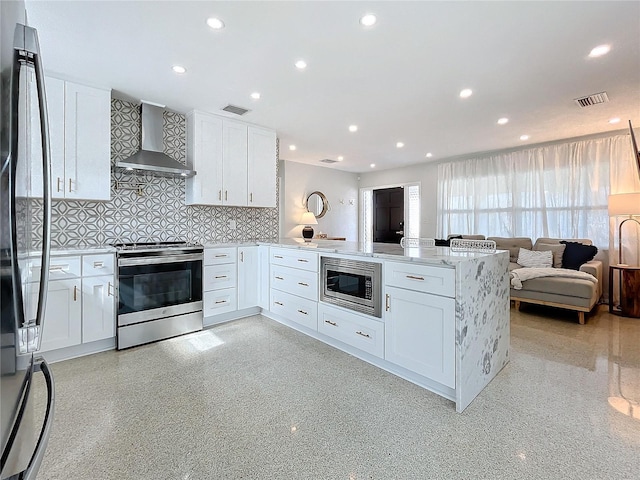 kitchen featuring stainless steel appliances, wall chimney range hood, backsplash, kitchen peninsula, and white cabinets