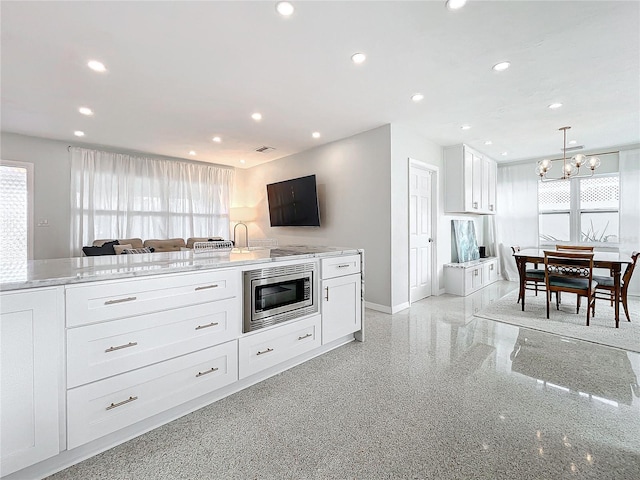 kitchen featuring stainless steel microwave, an inviting chandelier, hanging light fixtures, light stone counters, and white cabinetry