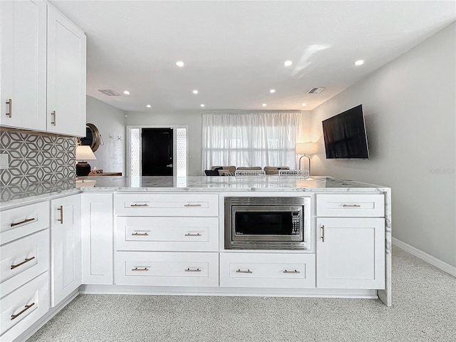 kitchen featuring kitchen peninsula, tasteful backsplash, white cabinetry, and stainless steel microwave