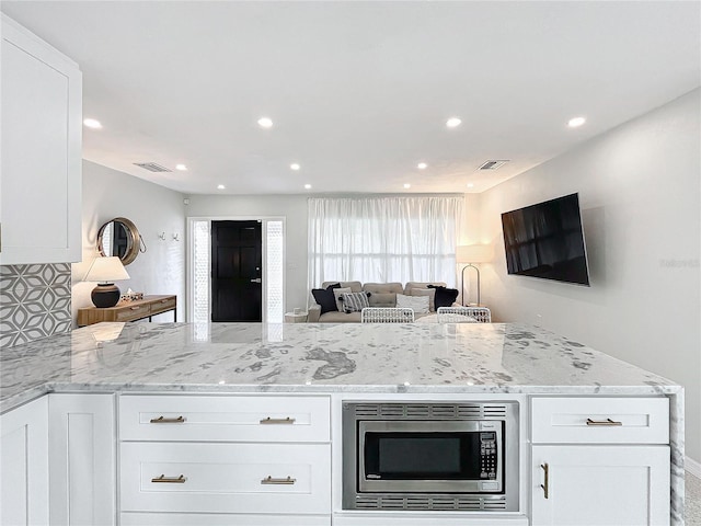 kitchen with white cabinetry, light stone counters, and stainless steel microwave