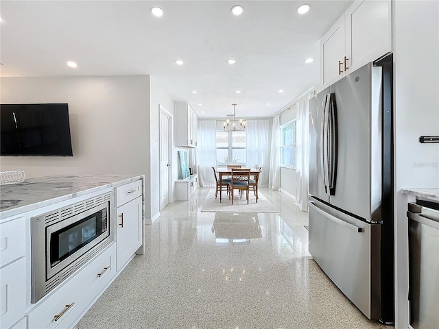 kitchen featuring pendant lighting, an inviting chandelier, light stone countertops, white cabinetry, and stainless steel appliances