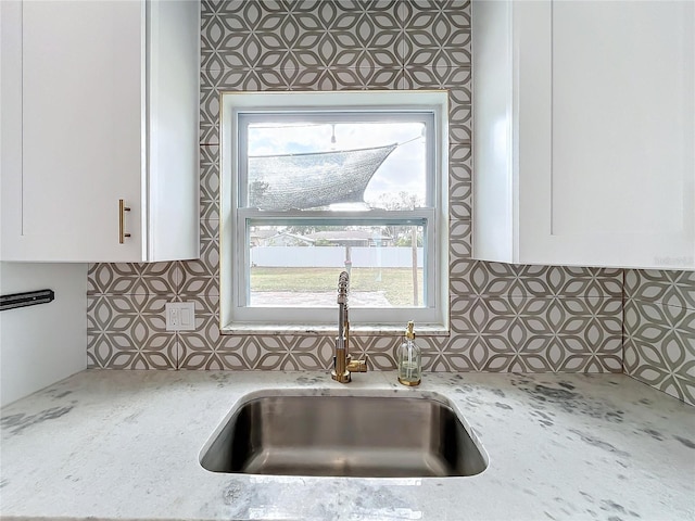 kitchen with white cabinets, backsplash, light stone counters, and sink