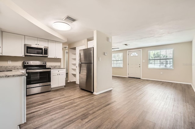 kitchen with light stone counters, hardwood / wood-style flooring, white cabinetry, and appliances with stainless steel finishes