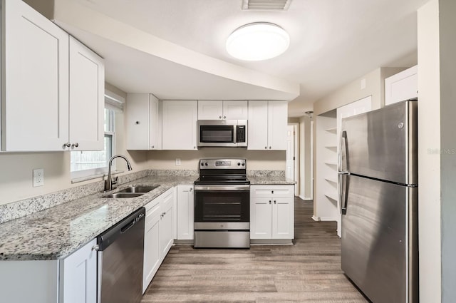 kitchen with appliances with stainless steel finishes, white cabinetry, sink, light hardwood / wood-style flooring, and light stone counters