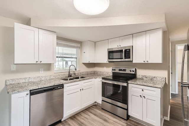 kitchen with sink, stainless steel appliances, white cabinetry, and light hardwood / wood-style floors