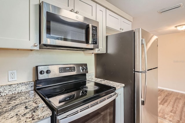 kitchen with light stone countertops, light hardwood / wood-style flooring, white cabinets, and appliances with stainless steel finishes