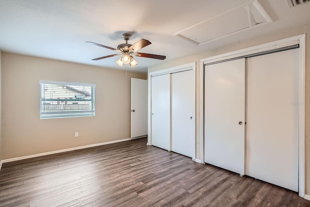 unfurnished bedroom with ceiling fan, dark wood-type flooring, and two closets