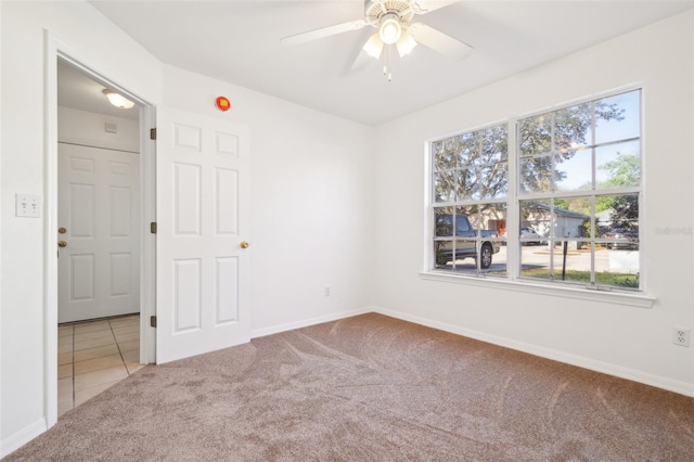 carpeted spare room featuring tile patterned floors, a ceiling fan, and baseboards