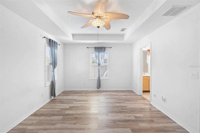 spare room with ceiling fan, a tray ceiling, and light hardwood / wood-style flooring