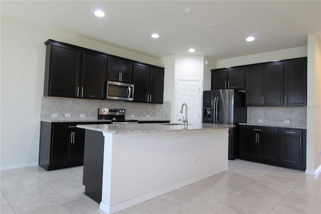 kitchen with light stone countertops, appliances with stainless steel finishes, light tile patterned flooring, sink, and an island with sink