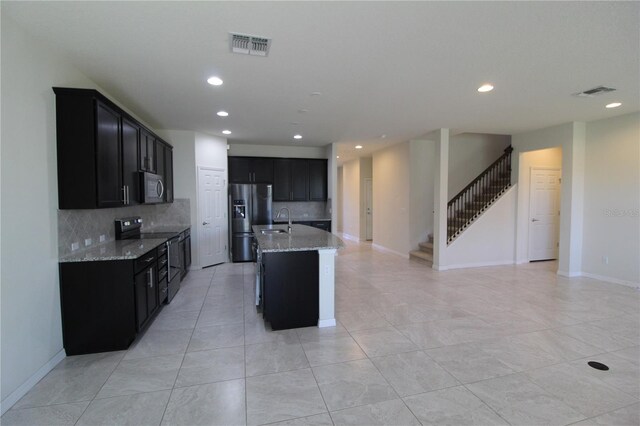 kitchen featuring light stone countertops, sink, stainless steel appliances, decorative backsplash, and a center island with sink