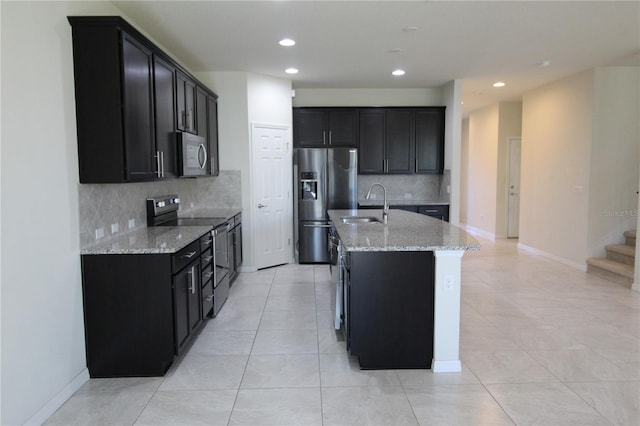 kitchen with a center island with sink, sink, appliances with stainless steel finishes, tasteful backsplash, and light stone counters