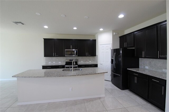 684 Bishop Bay Loop, Apopka, FL 32712 - kitchen with stainless steel microwave, black fridge, dark cabinets, light stone counters, and a center island with sink
