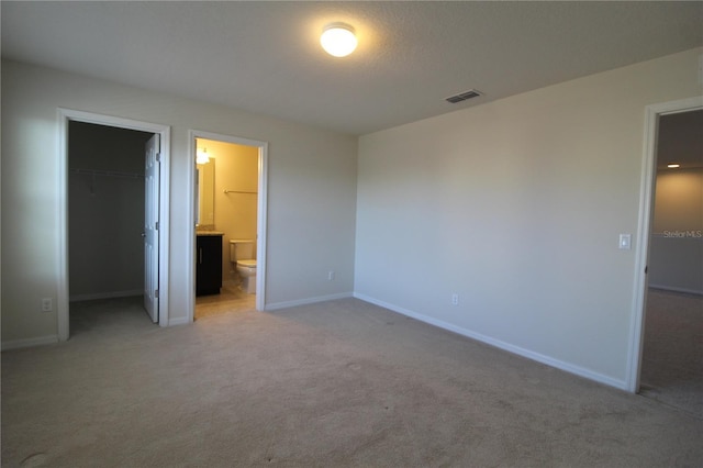 unfurnished bedroom with a walk in closet, light carpet, connected bathroom, and a closet