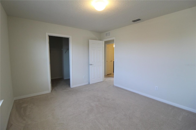 unfurnished bedroom featuring light colored carpet, a walk in closet, a textured ceiling, and a closet