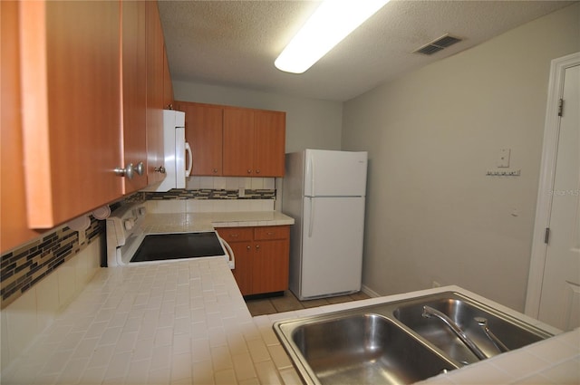 kitchen featuring tasteful backsplash, a textured ceiling, white appliances, sink, and tile countertops