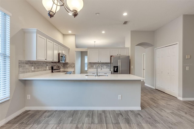 kitchen with kitchen peninsula, appliances with stainless steel finishes, sink, light hardwood / wood-style flooring, and white cabinetry