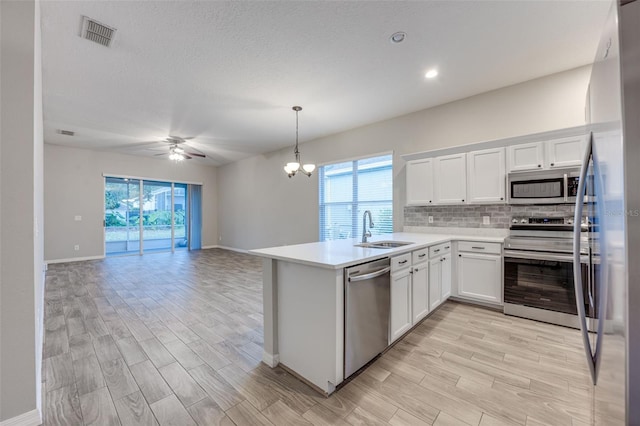 kitchen with sink, decorative backsplash, white cabinets, ceiling fan with notable chandelier, and appliances with stainless steel finishes