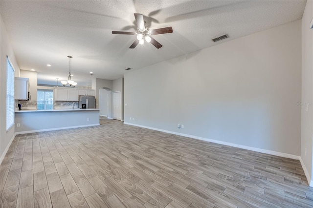 unfurnished living room with ceiling fan with notable chandelier, a textured ceiling, and light hardwood / wood-style flooring