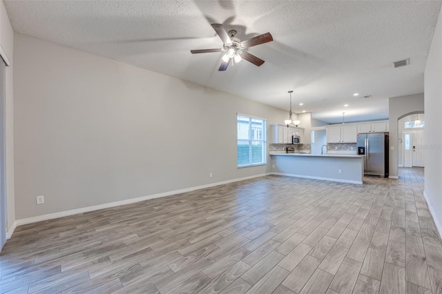 unfurnished living room with a textured ceiling, sink, ceiling fan with notable chandelier, and light wood-type flooring