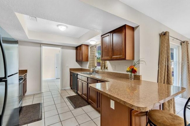 kitchen with kitchen peninsula, a kitchen bar, a tray ceiling, and stainless steel refrigerator