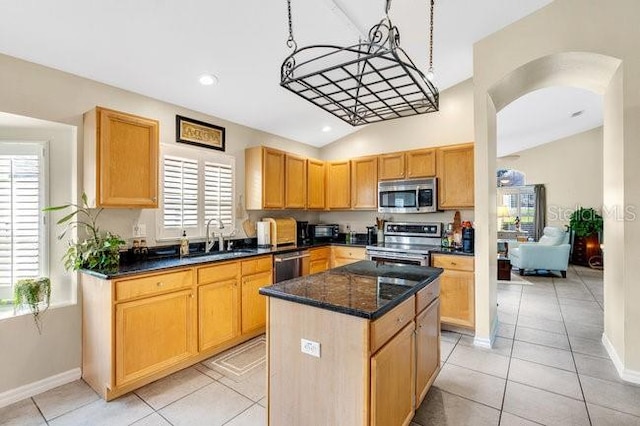 kitchen with stainless steel appliances, a center island, sink, light tile patterned floors, and dark stone countertops