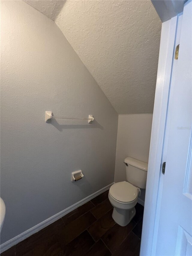 bathroom with a textured ceiling, hardwood / wood-style flooring, vaulted ceiling, and toilet