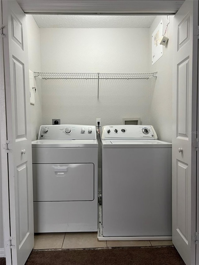 clothes washing area with washer and dryer, light tile patterned floors, and a textured ceiling