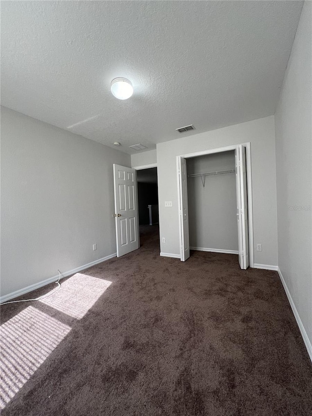 unfurnished bedroom featuring dark carpet, a textured ceiling, and a closet