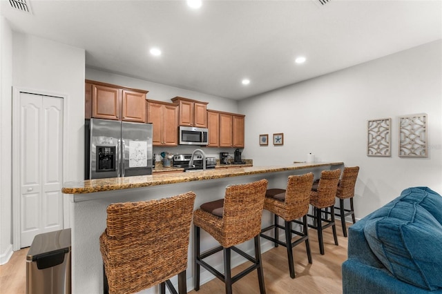 kitchen featuring light stone counters, a kitchen island with sink, a breakfast bar, appliances with stainless steel finishes, and light wood-type flooring