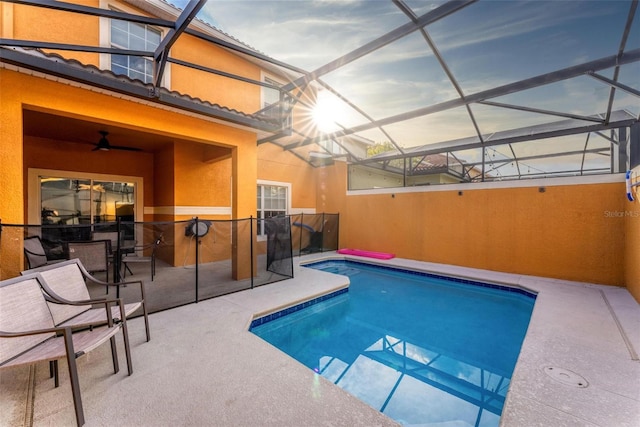 pool at dusk featuring glass enclosure, ceiling fan, and a patio