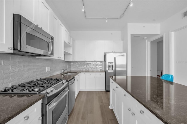 kitchen featuring rail lighting, backsplash, white cabinets, dark stone counters, and appliances with stainless steel finishes