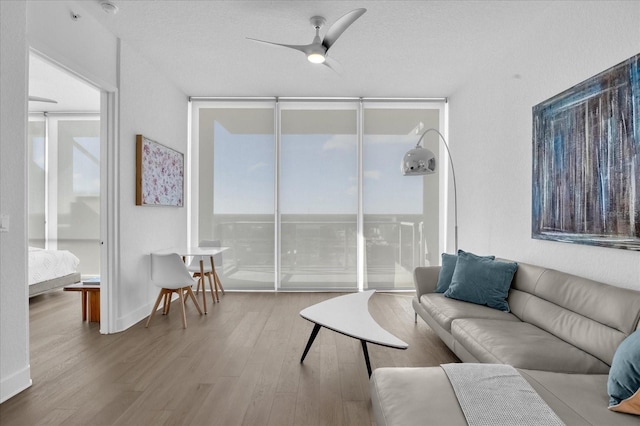 living room featuring ceiling fan, a wall of windows, and plenty of natural light