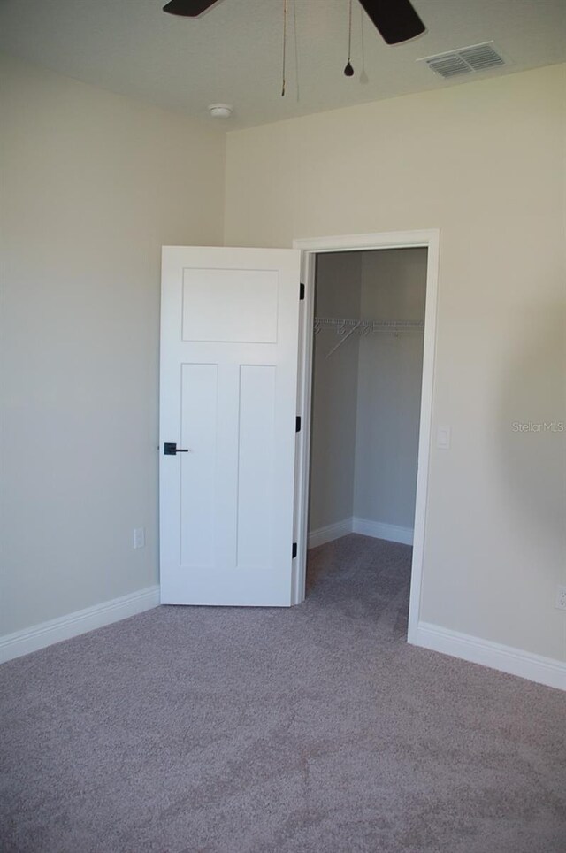 unfurnished bedroom featuring a walk in closet, a closet, ceiling fan, and carpet flooring