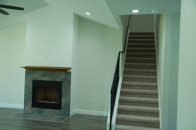 staircase with hardwood / wood-style flooring, ceiling fan, and a tiled fireplace