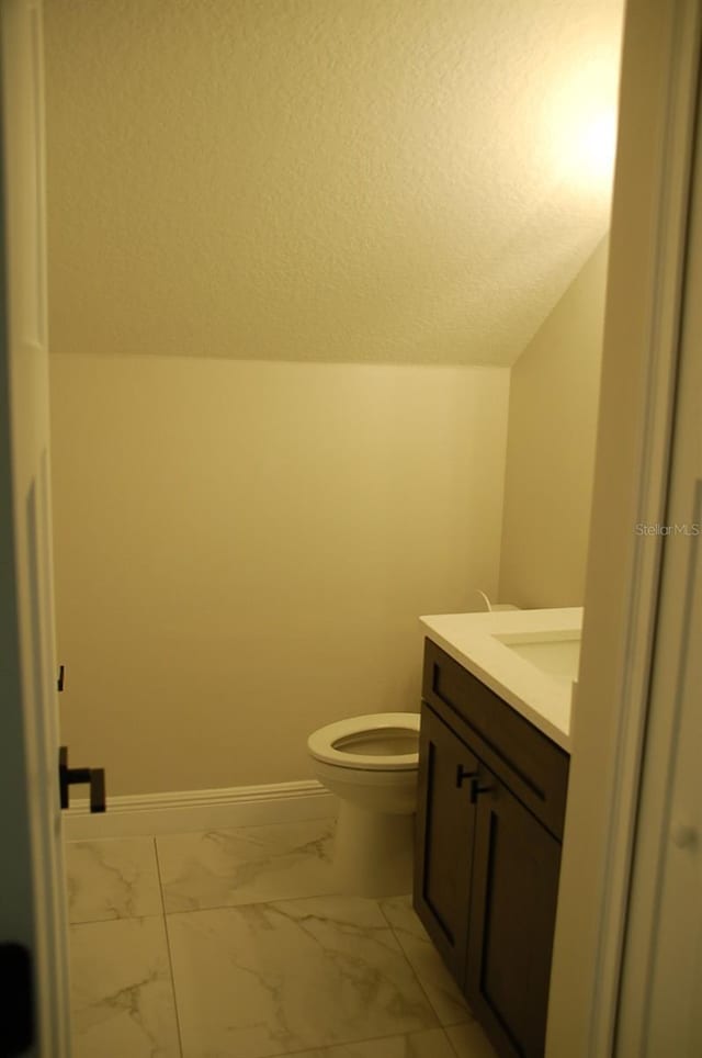 bathroom with vanity, toilet, vaulted ceiling, and a textured ceiling