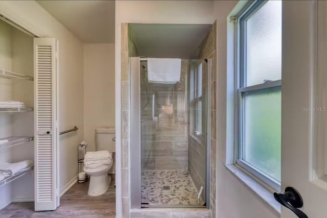 bathroom featuring hardwood / wood-style floors, a healthy amount of sunlight, an enclosed shower, and toilet